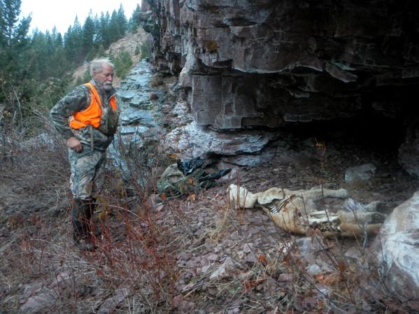 A man in an orange vest is standing next to a skeleton in the woods.