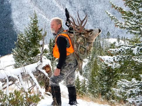 A man is carrying a large deer on his back in the snow.