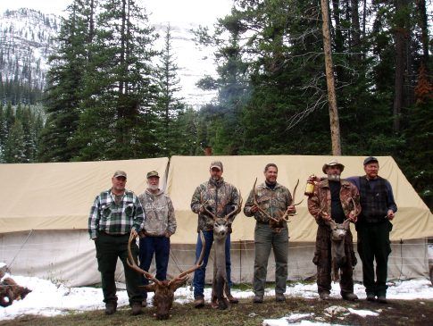 A group of men standing in front of a tent holding deer antlers