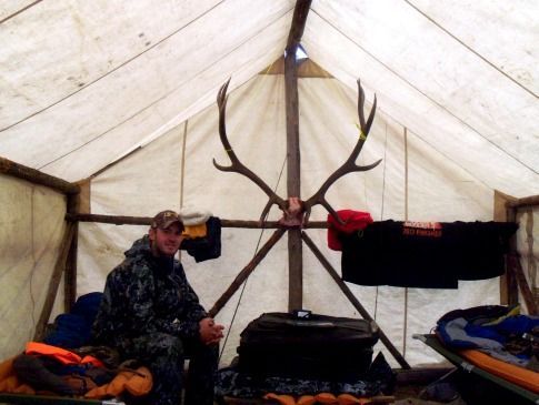 A man sits in a tent with antlers hanging from the ceiling