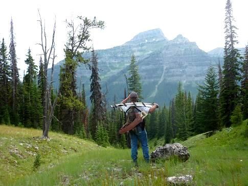 A man is standing in a grassy field carrying a backpack and a surfboard.