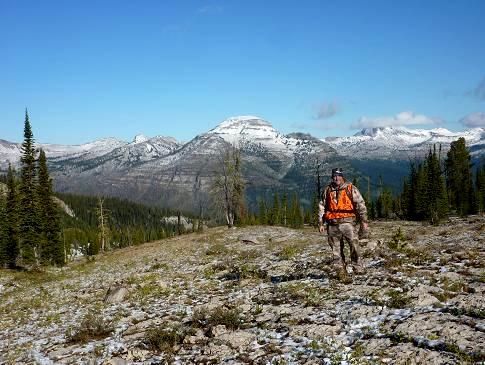 A man in an orange vest is walking on a rocky trail in the mountains.