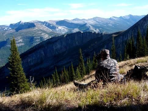 A person is sitting on top of a grassy hill overlooking a mountain range.