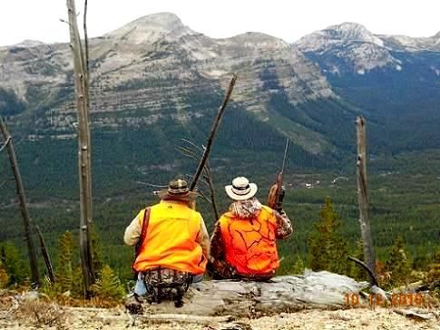 Two men are sitting on a rock looking at a mountain range.