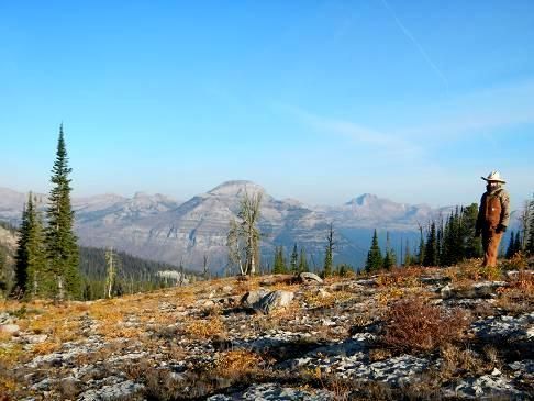 A man is standing on top of a rocky hill with mountains in the background.