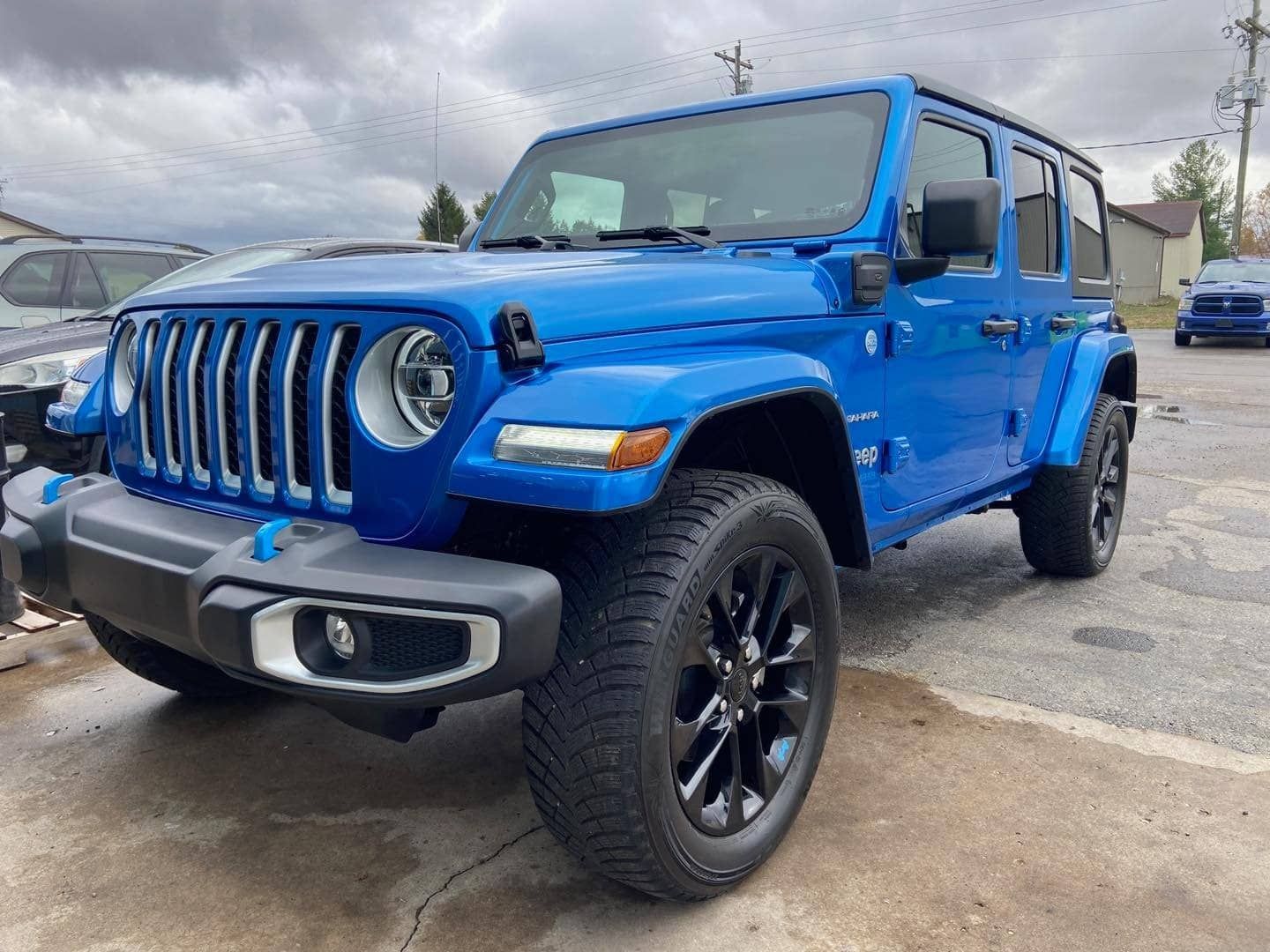Blue Jeep Wrangler parked on asphalt on a cloudy day.