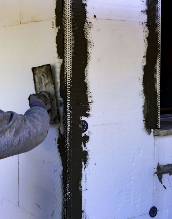 Un operaio utilizza una cazzuola per applicare la malta su un profilo angolare forato installato su un pannello isolante in schiuma bianca.