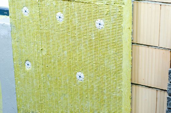 Un pannello isolante in lana minerale gialla fissato a un muro di mattoni con tasselli circolari bianchi.