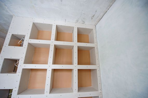 Una griglia di nove vani in cartongesso in fase di costruzione, inseriti in una stanza non rifinita con pareti grigie e cavi elettrici a vista.