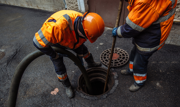 Two workers in orange safety gear cleaning a manhole in an urban setting.