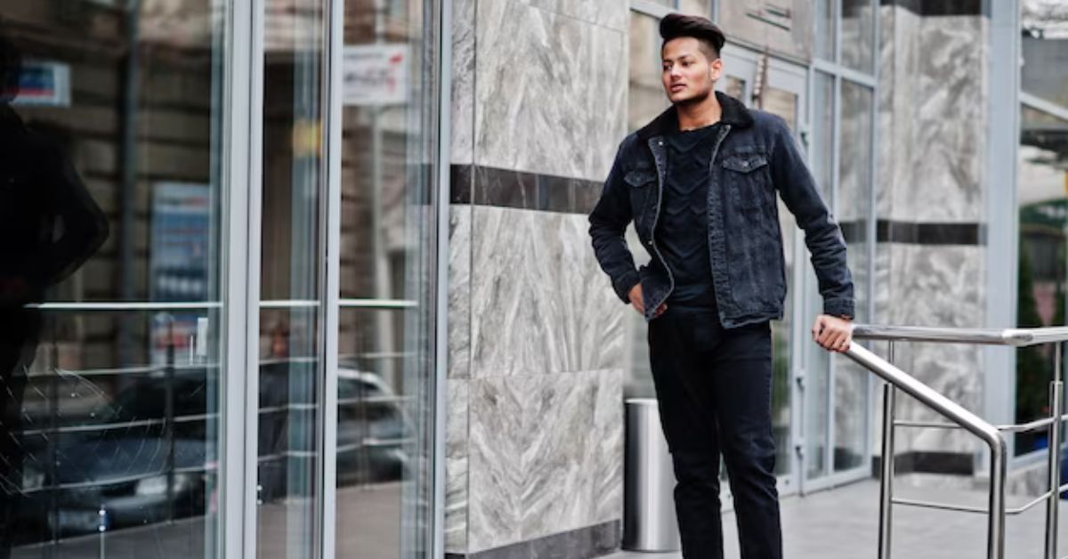 A man in a denim jacket is leaning on a railing in front of a building.