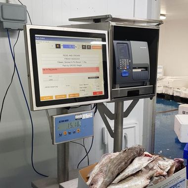 A computer monitor is sitting on top of a scale next to a box of fish.