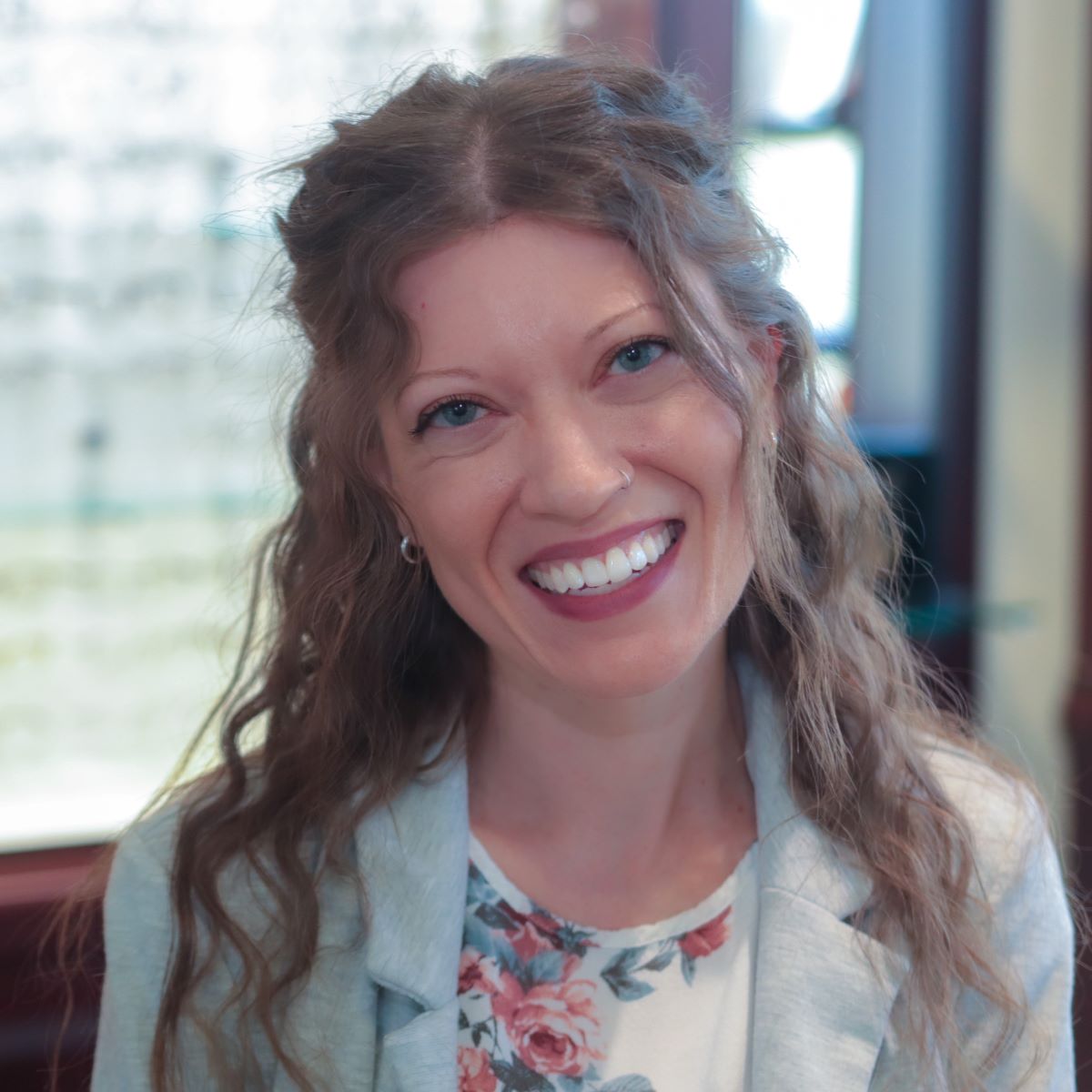A woman with long hair is smiling and wearing a floral shirt.