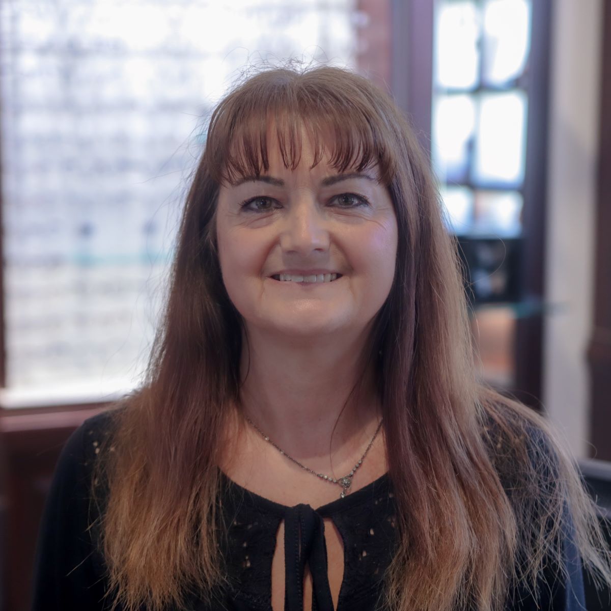 A woman with long hair is smiling for the camera in front of a display of glasses.