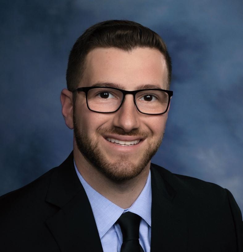 A man wearing glasses and a suit and tie is smiling for the camera.