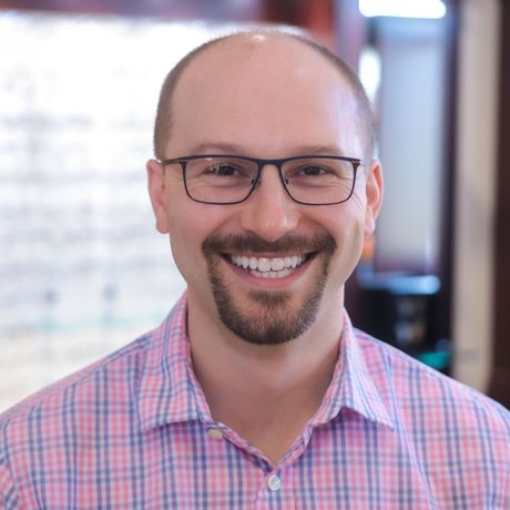 A man wearing glasses and a plaid shirt smiles for the camera