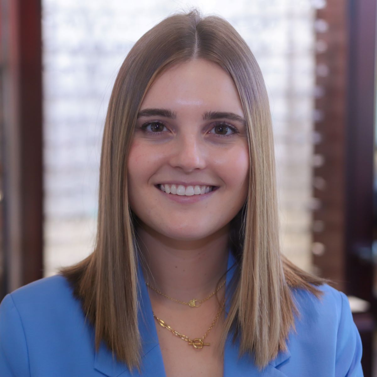 A woman wearing a blue jacket and a gold necklace is smiling for the camera.