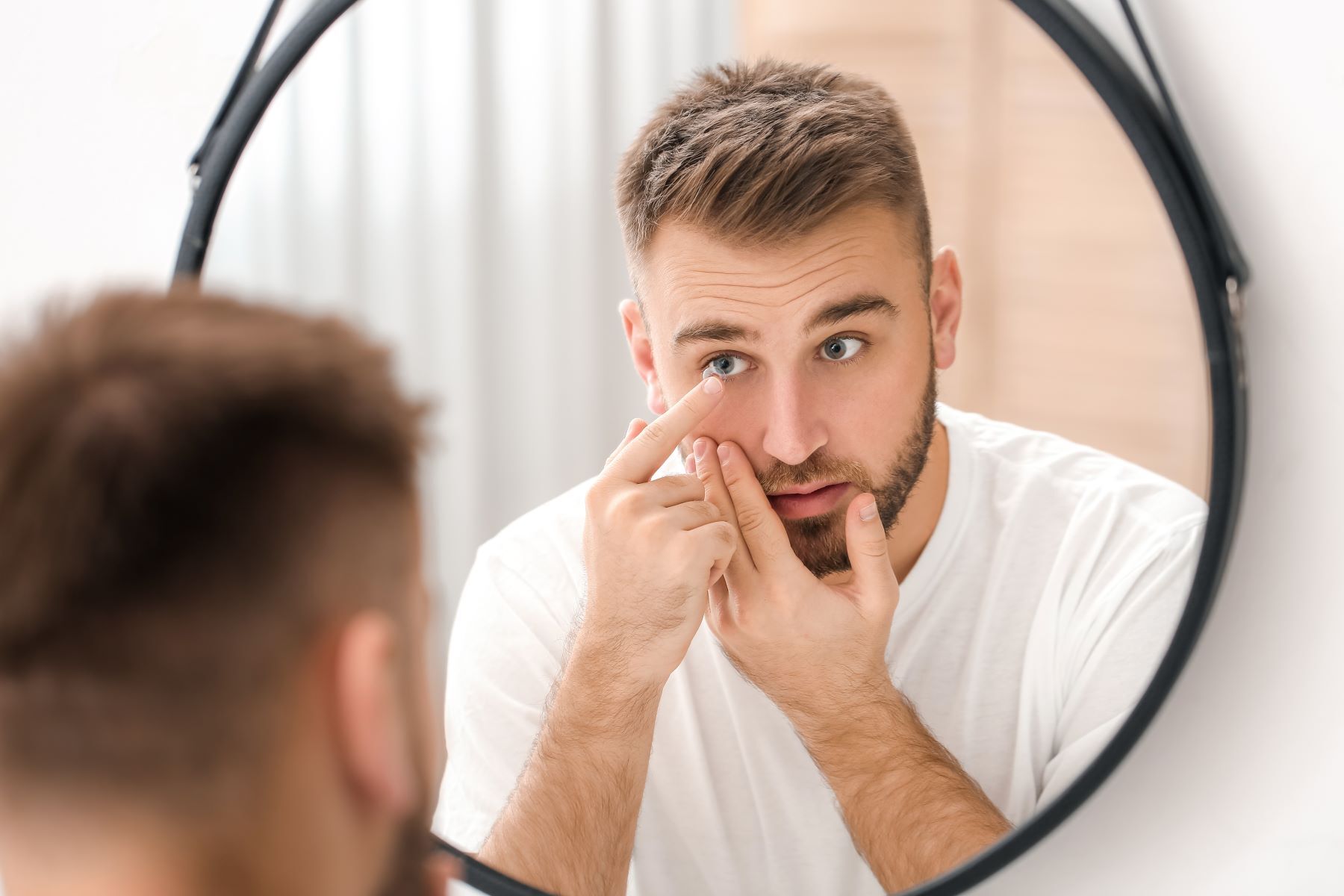 A man is applying contact lenses in front of a mirror.