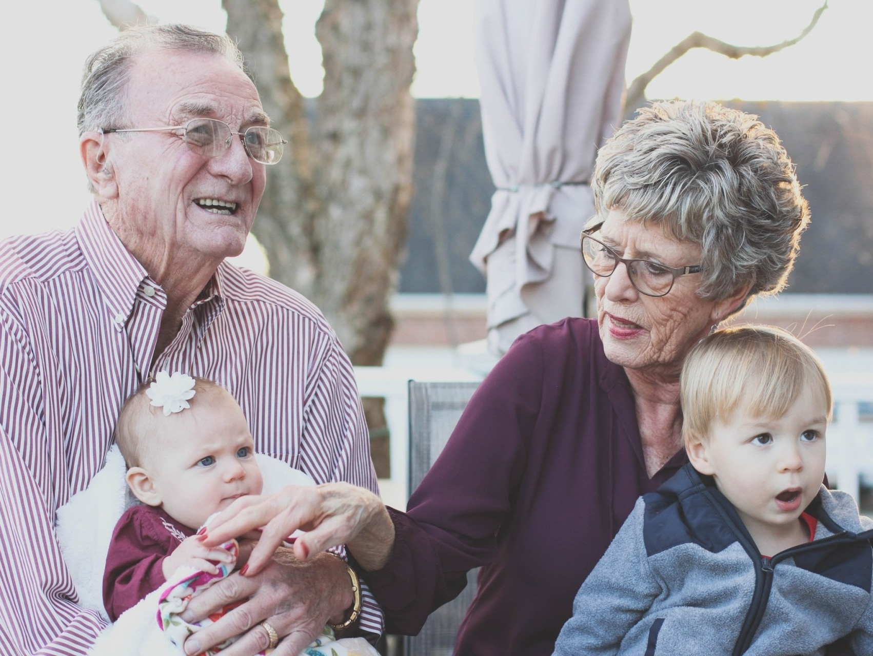 An elderly couple is holding two children while sitting on a bench.