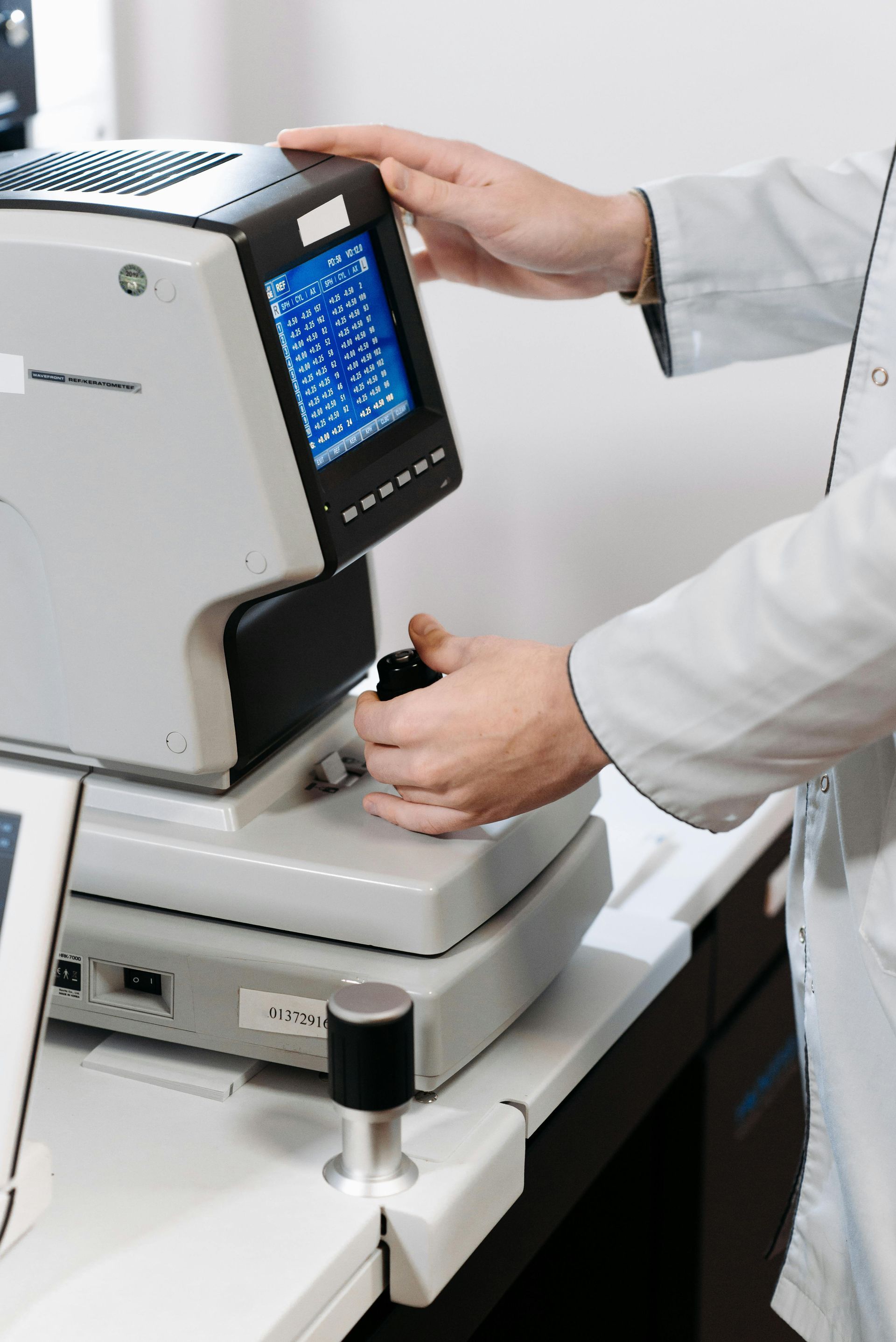 A healthcare professional in a white coat uses an eye examination device in a clinic.