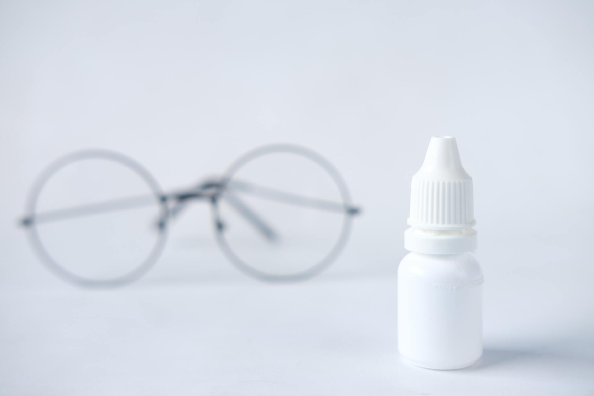 A pair of glasses and a bottle of eye drops on a table.