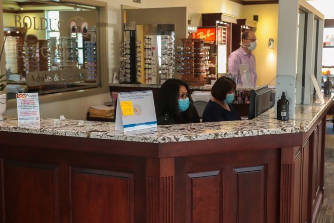 Two women wearing masks are sitting at a counter in an optical shop.