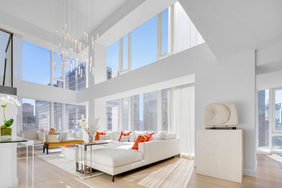 Bright modern living room with white sofas, orange accents, and tall windows with city views