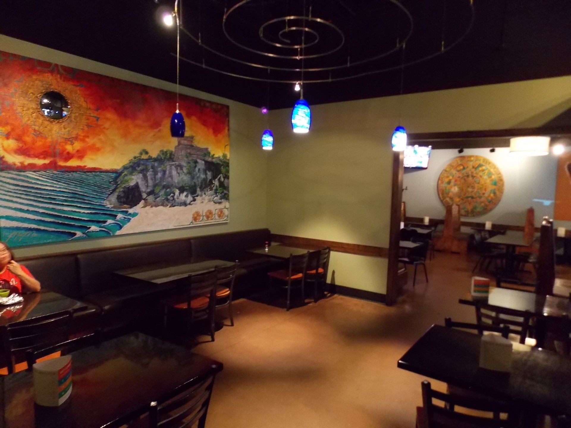 Restaurant interior with mural of ocean scene, tables, and blue pendant lights.