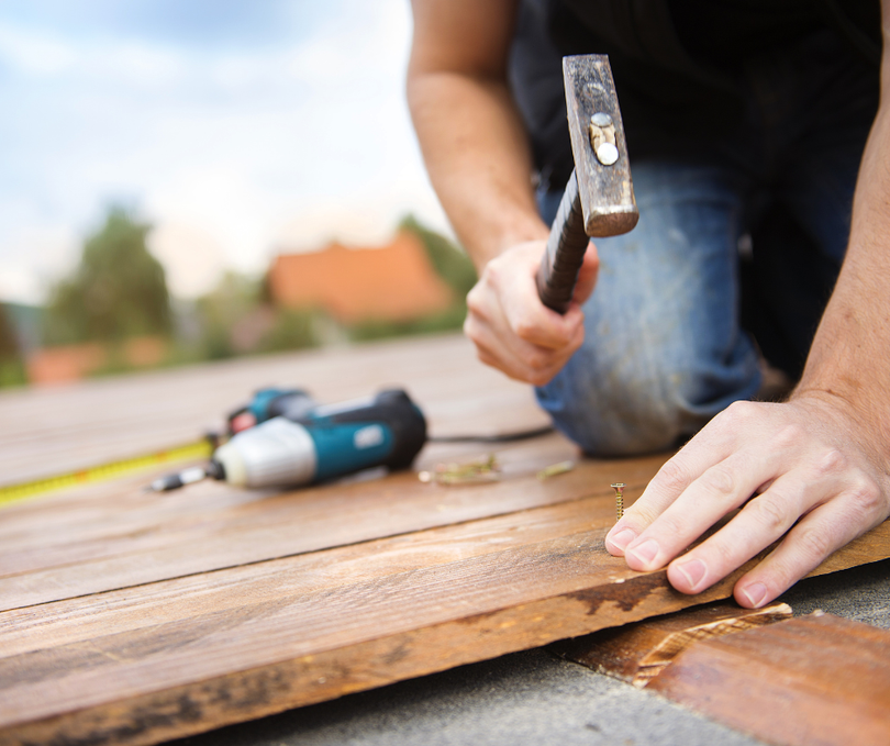 A man wearing a hard hat is using a jigsaw to cut a piece of wood.