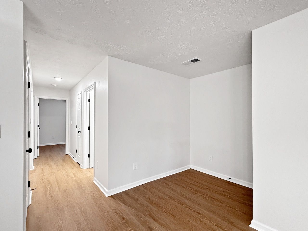 Empty white room with wood floors and hallway doors, lit by natural light