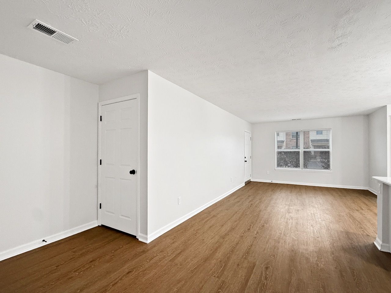 Empty white room with wood floors, a closed door, and a window at the far end.