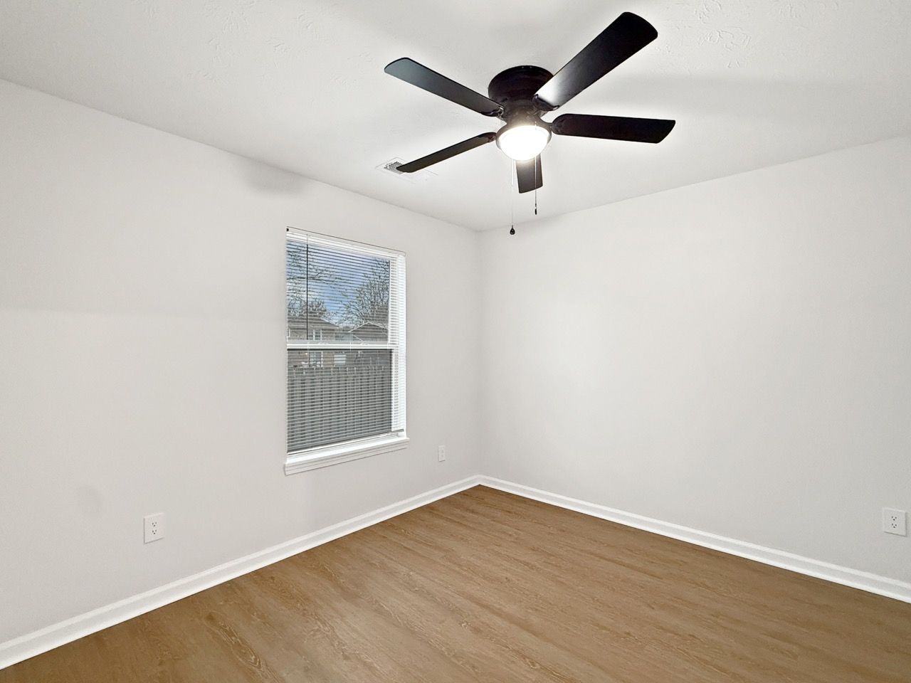Empty white bedroom with a ceiling fan, window, and wood-look floor