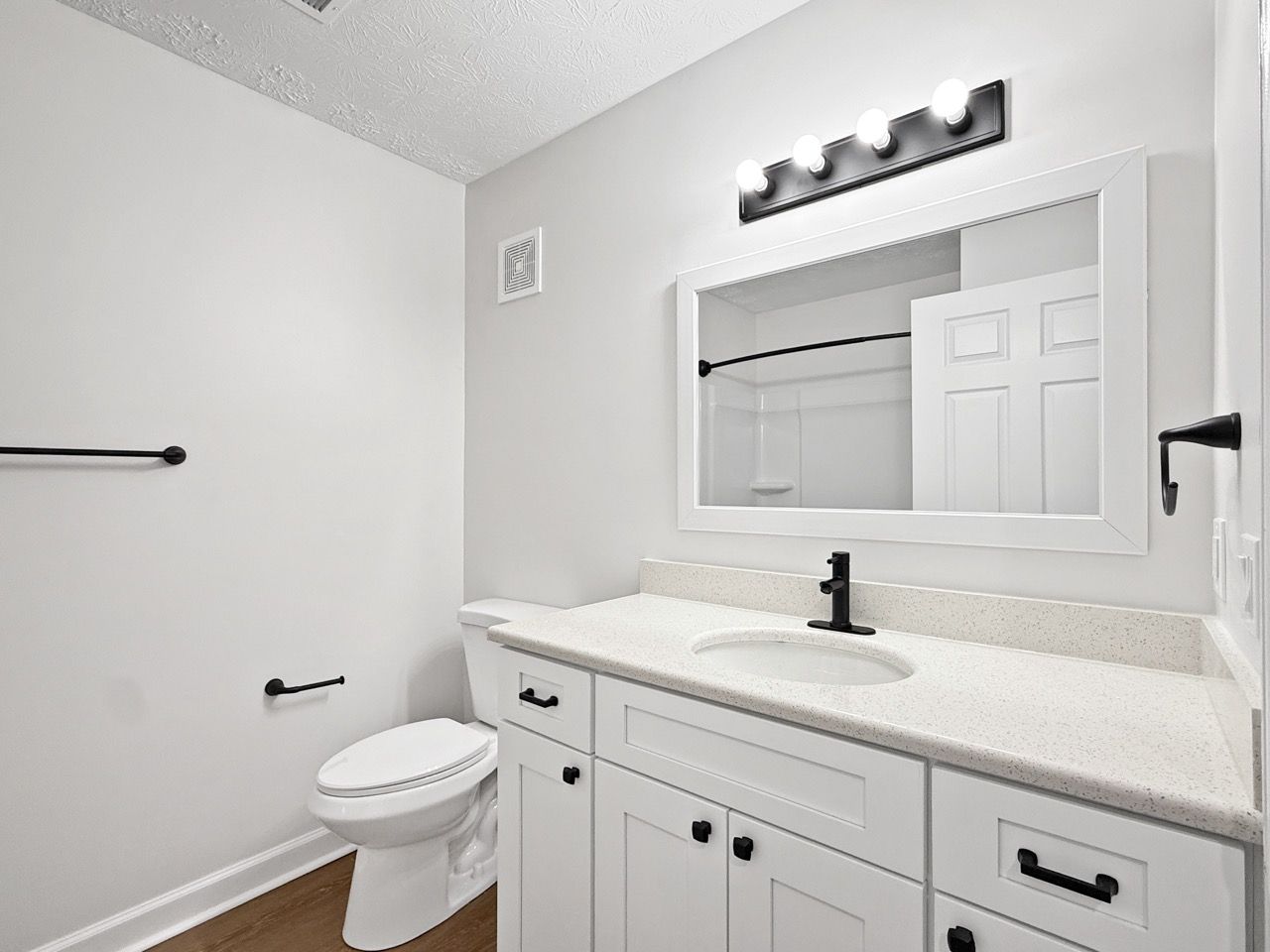 Small white bathroom with toilet, vanity sink, mirror, and black fixtures