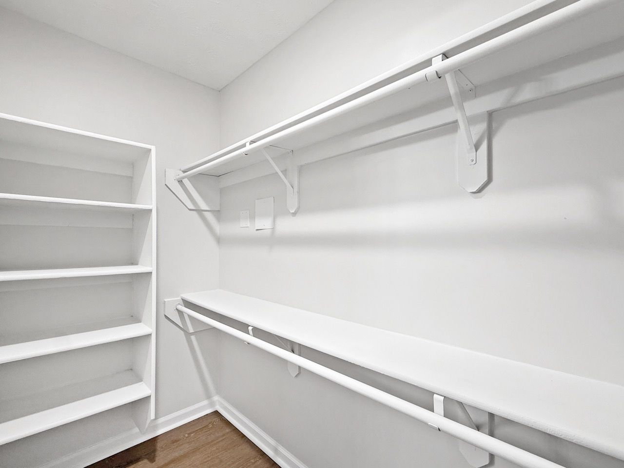 Empty white walk-in closet with shelves on the left and hanging rods on the right