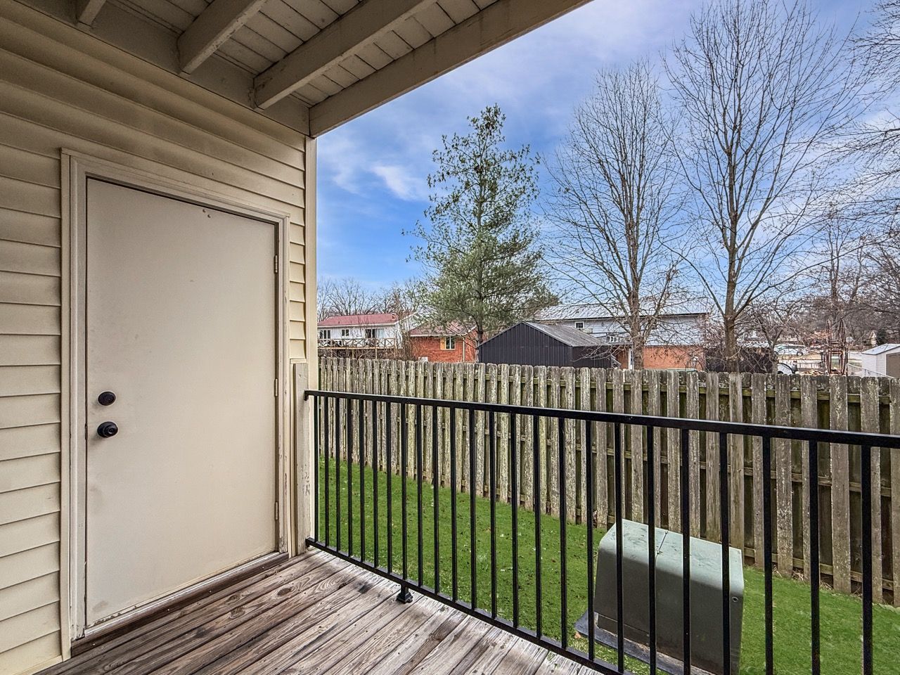 Balcony with white door, black railing, green lawn, and trees under a blue sky