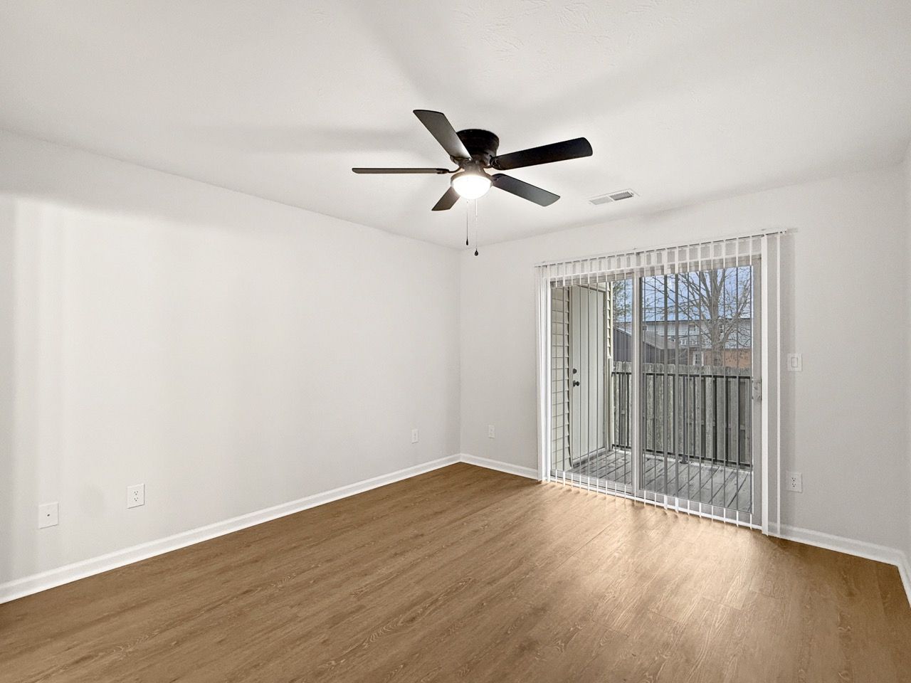 Empty white room with wood floors, ceiling fan, and sliding glass doors to a balcony.