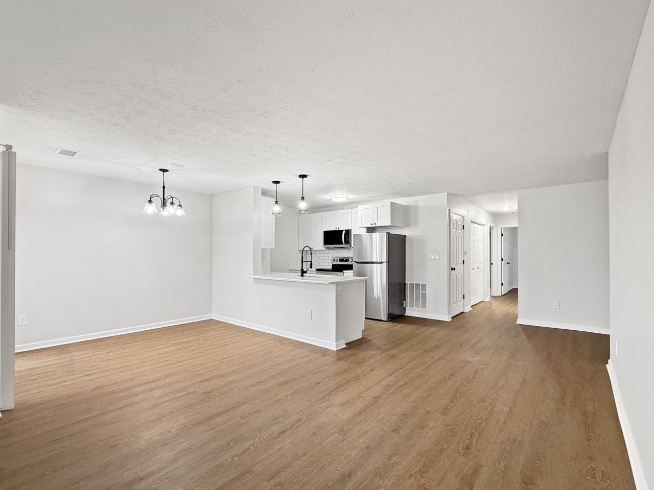 Bright empty open-plan living room and kitchen with white walls and light wood floors