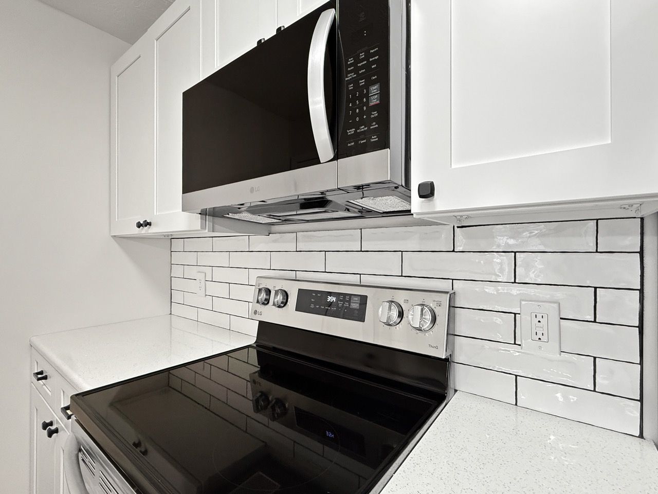 Modern kitchen with black stove, microwave, white cabinets, and white subway tile backsplash