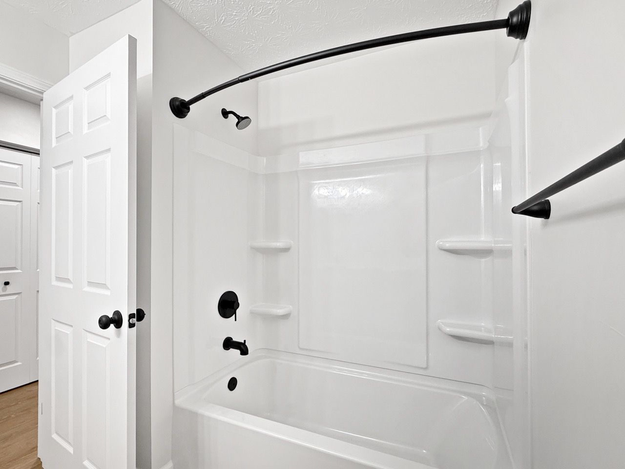 White bathroom with a tub-shower, black fixtures, corner shelves, and a glass shower door.