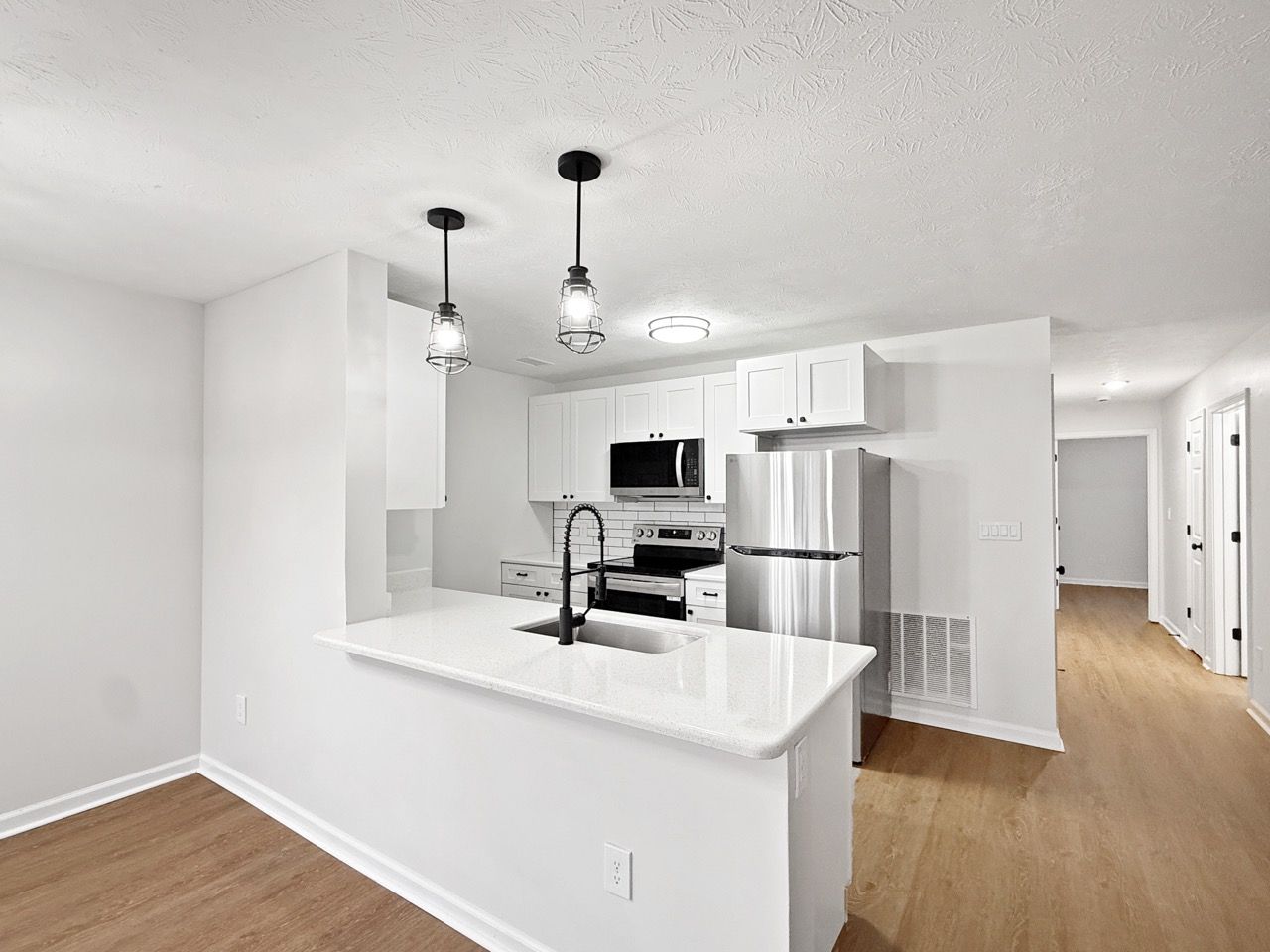 Bright white kitchen with stainless steel appliances, island, pendant lights, and wood floors.