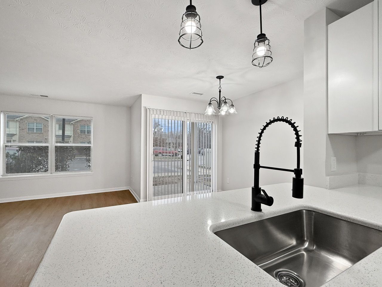 Bright open kitchen with white counters, black faucet, pendant lights, and view into a living area with sliding doors.