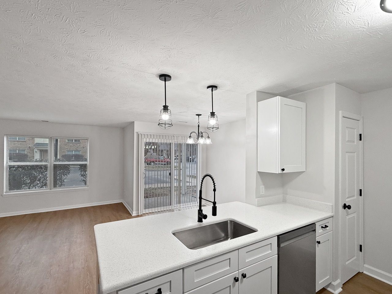 Bright open kitchen with white cabinets, stainless sink, and adjacent dining area with sliding glass doors.