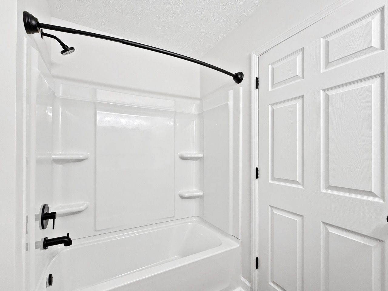 White shower-tub combo with black curtain rod and chrome fixtures in a bathroom.