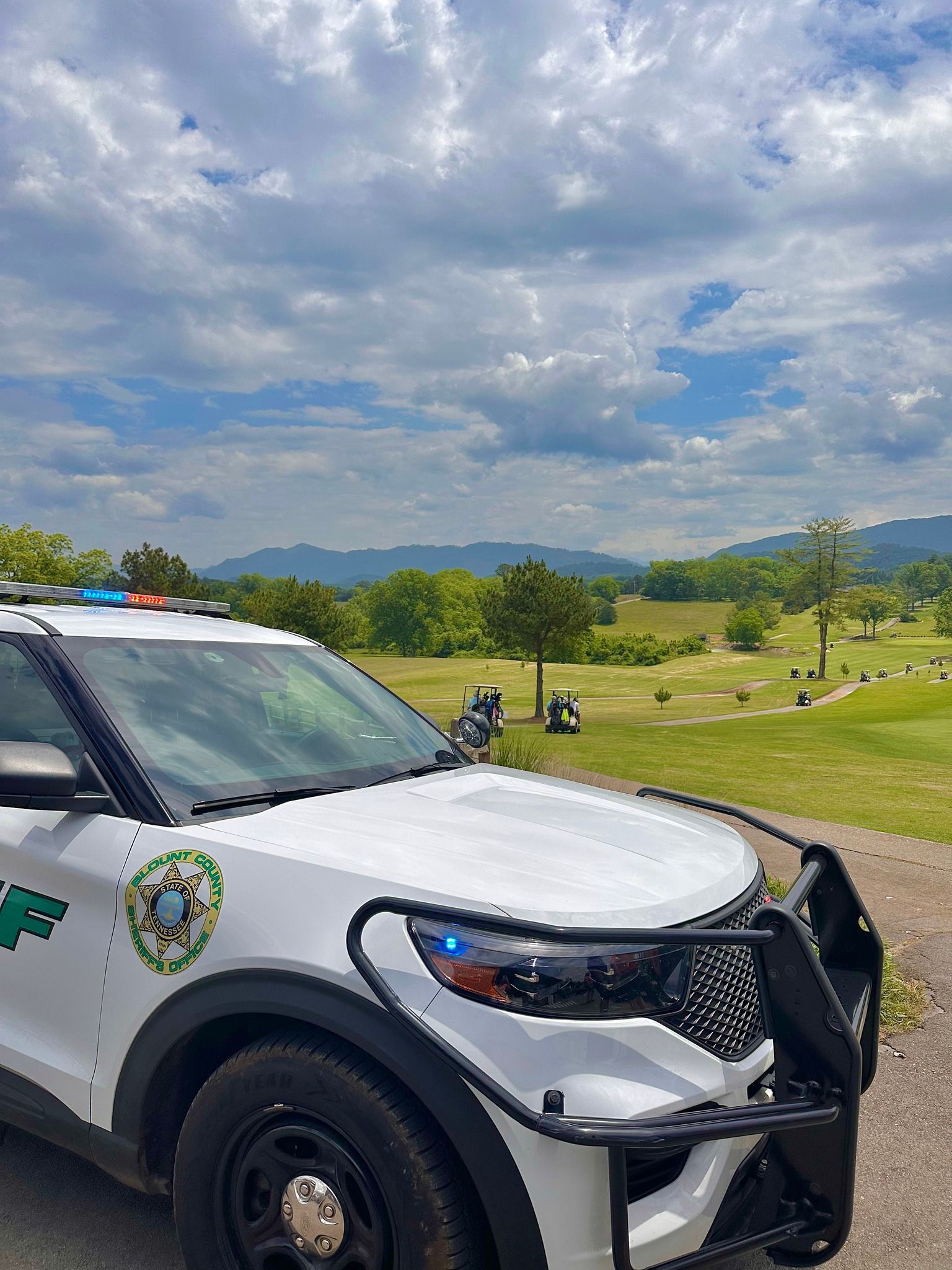 A white police car is parked on the side of a road in front of a field.