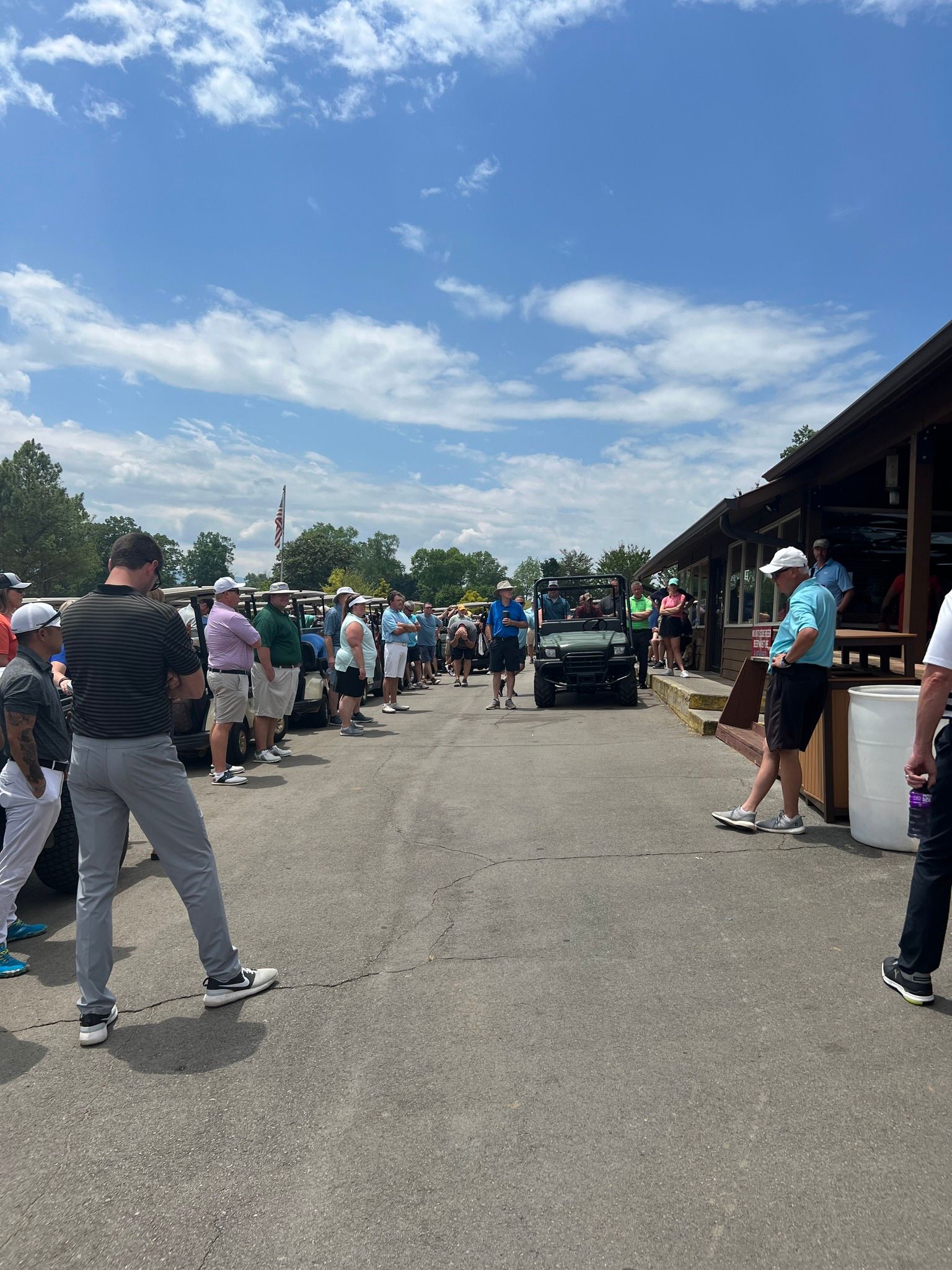 A group of people are standing in a parking lot at a golf course.