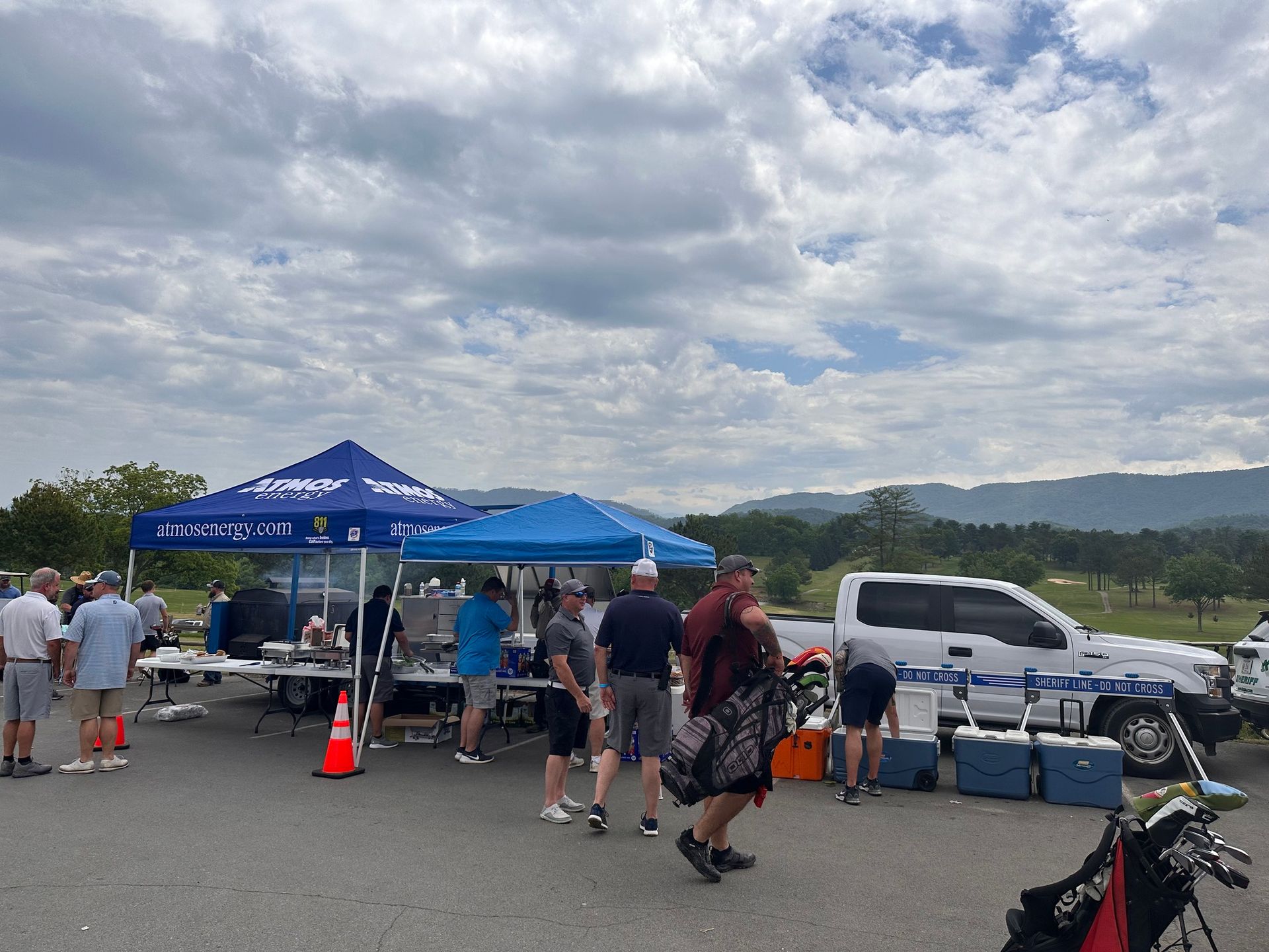A group of people are standing in a parking lot with tents and coolers.