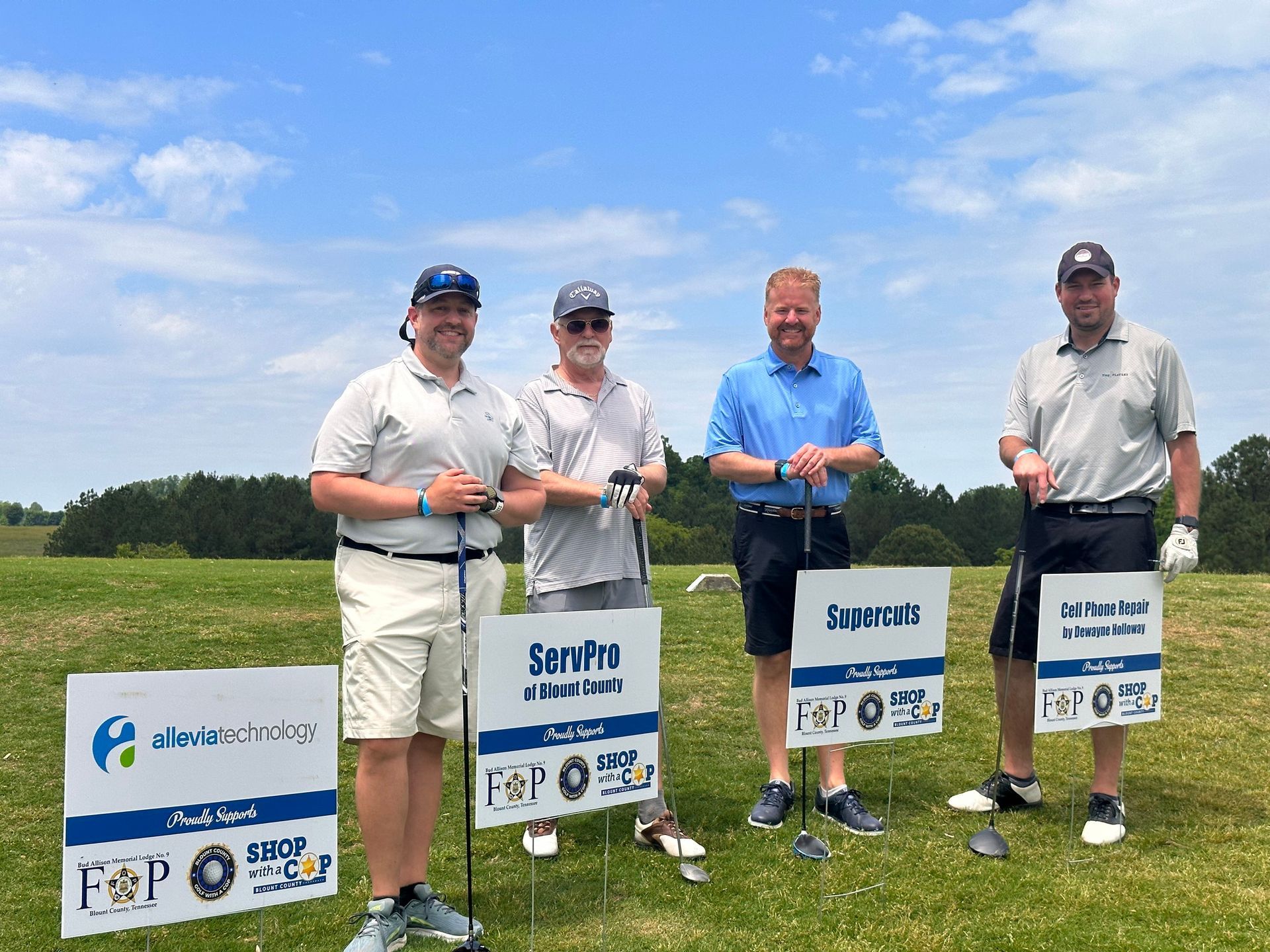 A group of men are standing on a golf course holding golf clubs and signs.