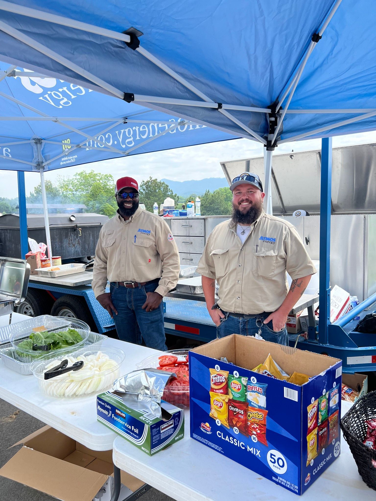 Two men are standing at a table under a blue tent.