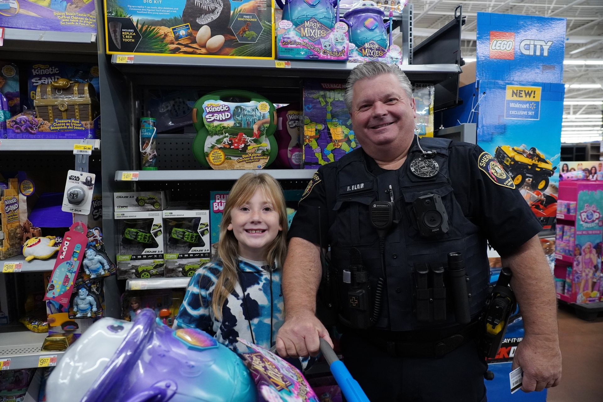 A police officer is standing next to a little girl in a shopping cart in a store.