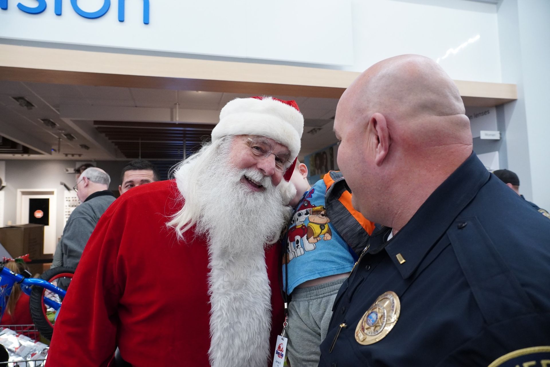 A man dressed as santa claus is talking to a police officer in a store.